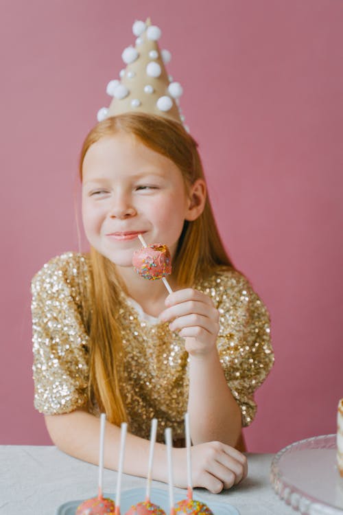 A Young Girl Wearing a Party Hat Eating Candy · Free Stock Photo