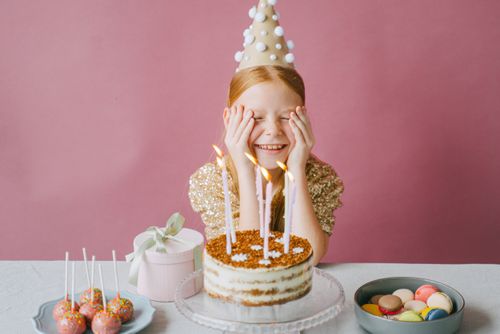 Free A young girl celebrates her birthday with cake and lollipops, wearing a party hat and gold dress. Stock Photo