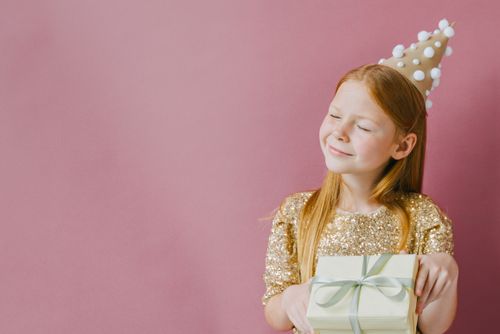 Free A smiling girl in a gold dress enjoys her birthday with a gift against a pink background. Stock Photo