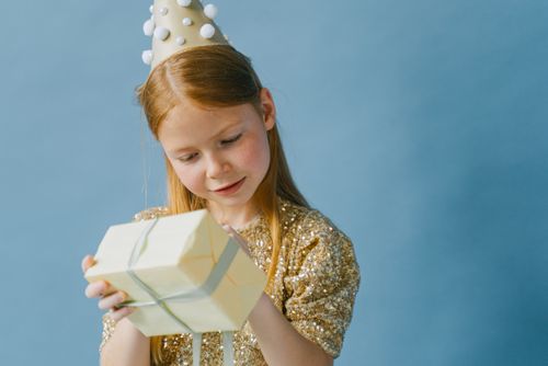 Free A red-haired girl in a party hat enjoys her birthday gift against a blue background. Stock Photo