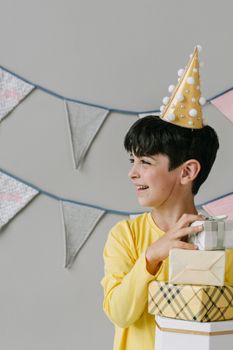 Smiling boy in party hat holds gifts at a birthday celebration.