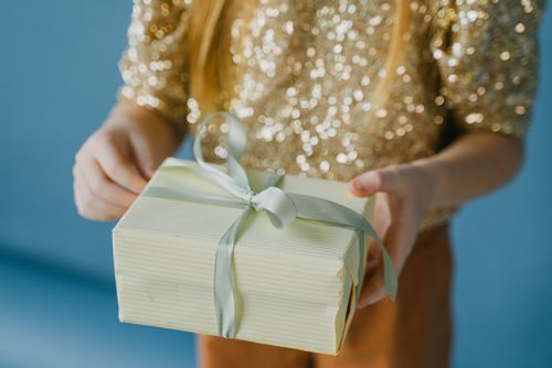 Free A close-up of a gift wrapped in elegant paper held by a child in a sparkling top. Stock Photo