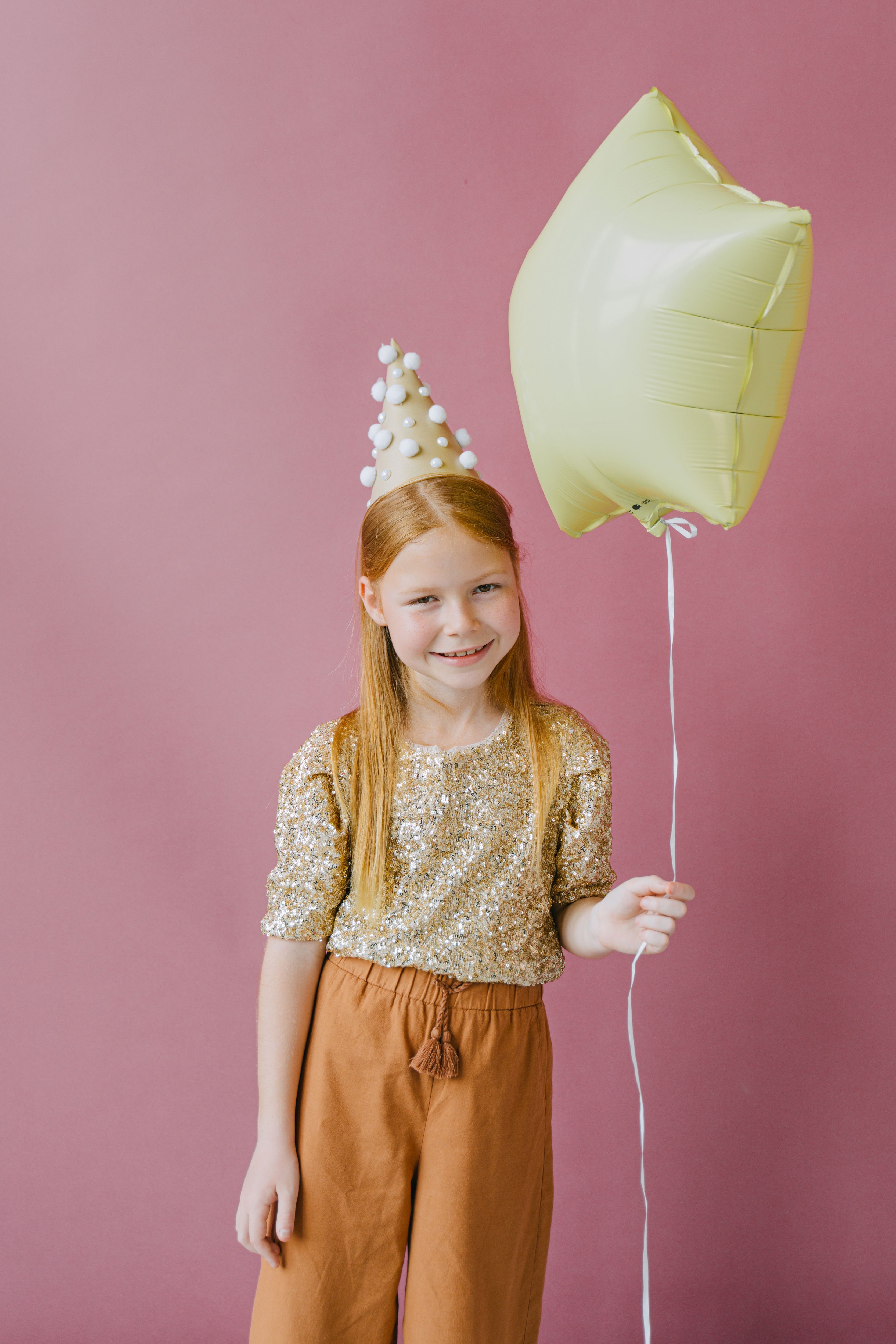 First birthday balloon decor ideas with birthday girl holding a balloon against a pink backdrop