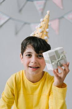 Excited boy in a party hat holding a wrapped gift, celebrating his birthday with joy.
