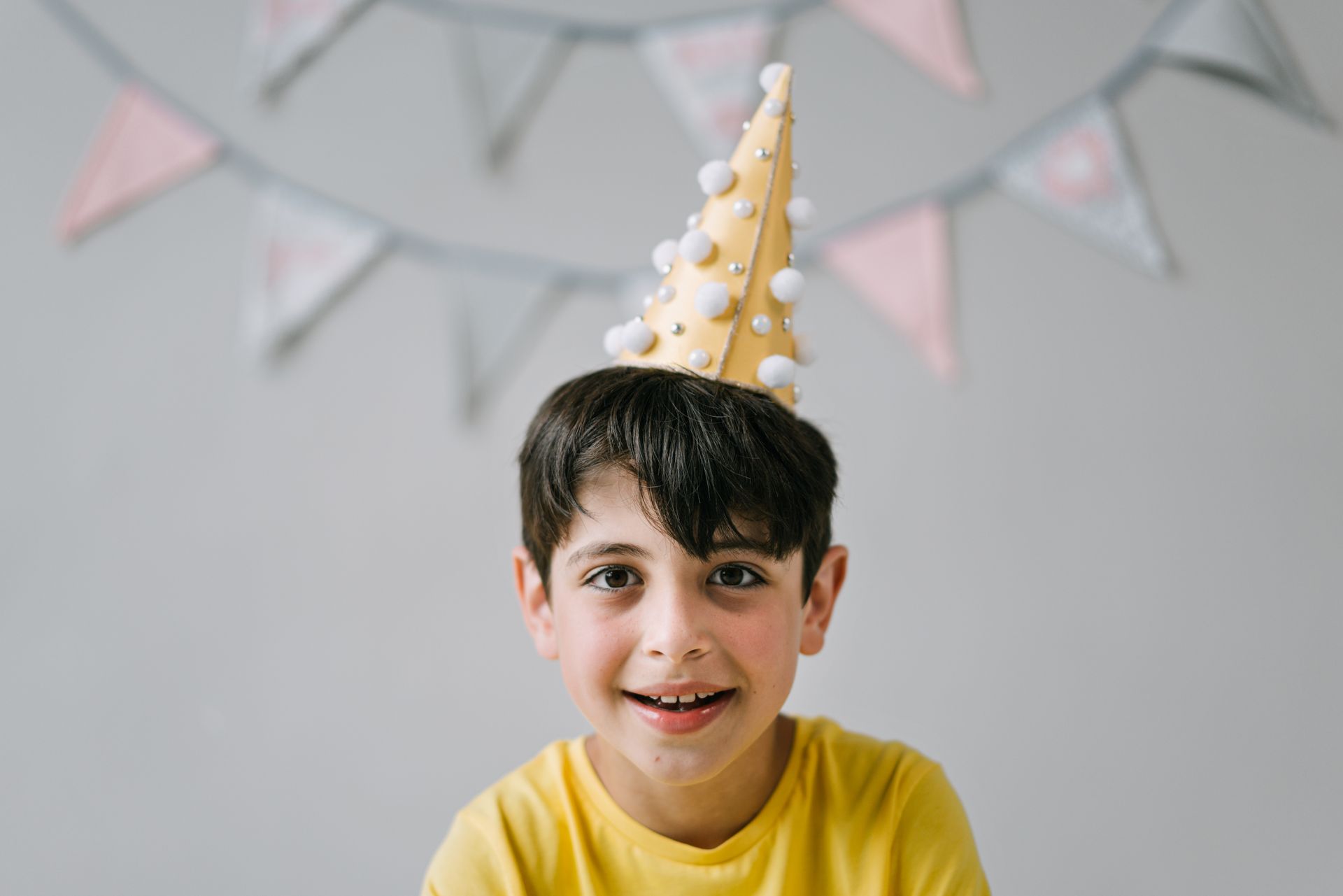A cheerful child wearing a party hat with bunting decoration in the background.