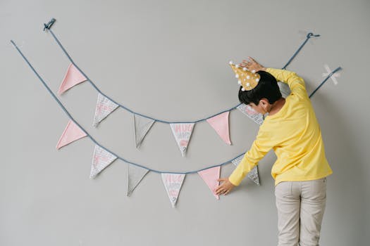 A young boy in a yellow shirt adjusts birthday bunting on a wall during a festive celebration.