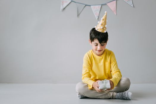 Young boy in party hat opening a birthday gift in a festive indoor setting.