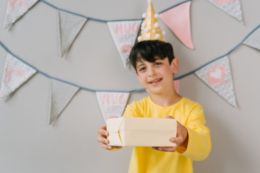 A happy child in a party hat holding a gift amid colorful birthday decorations.