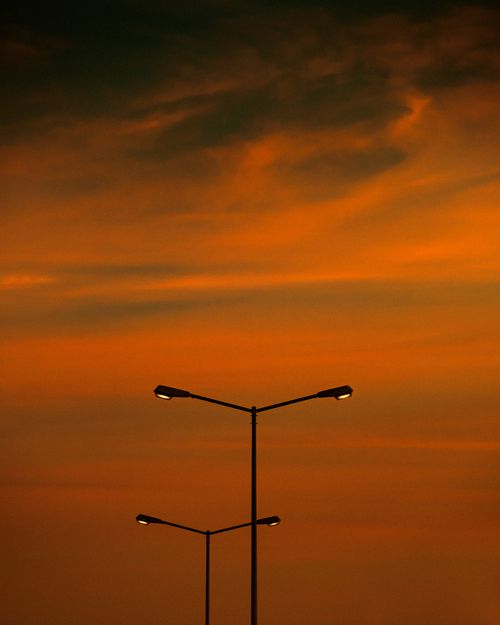 Free Vertical shot of streetlights silhouetted against a vibrant orange sunset sky, creating a dramatic urban scene. Stock Photo