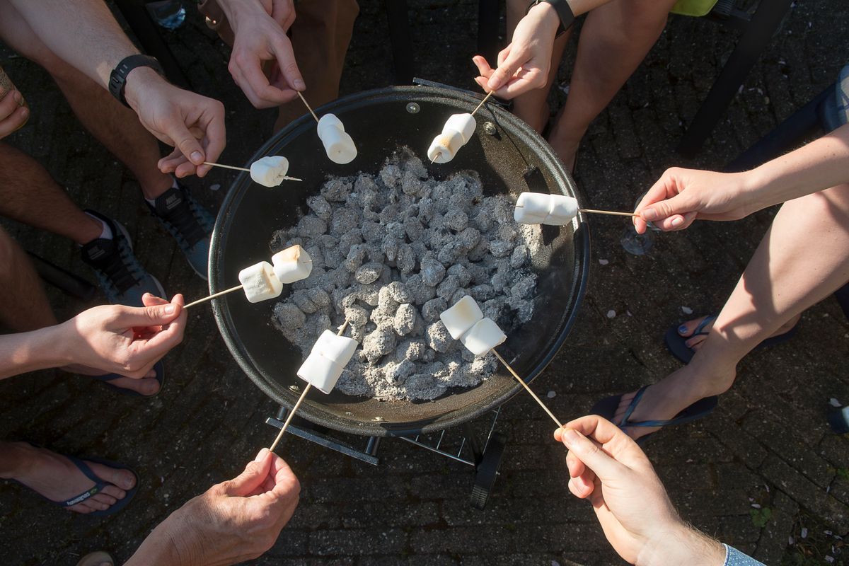 Close-up of hands roasting marshmallows over a charcoal grill, creating a lively outdoor party atmosphere.