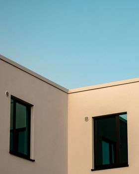 Contemporary building exterior featuring glass windows and minimalist design against a blue sky.