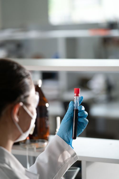 Free Scientist in lab coat examines a blood sample in test tube, focusing on research. Stock Photo