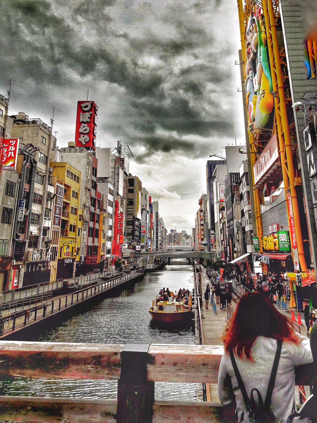 Bustling Dotonbori scene capturing tour boats and shoppers under dramatic skies in Osaka Japan