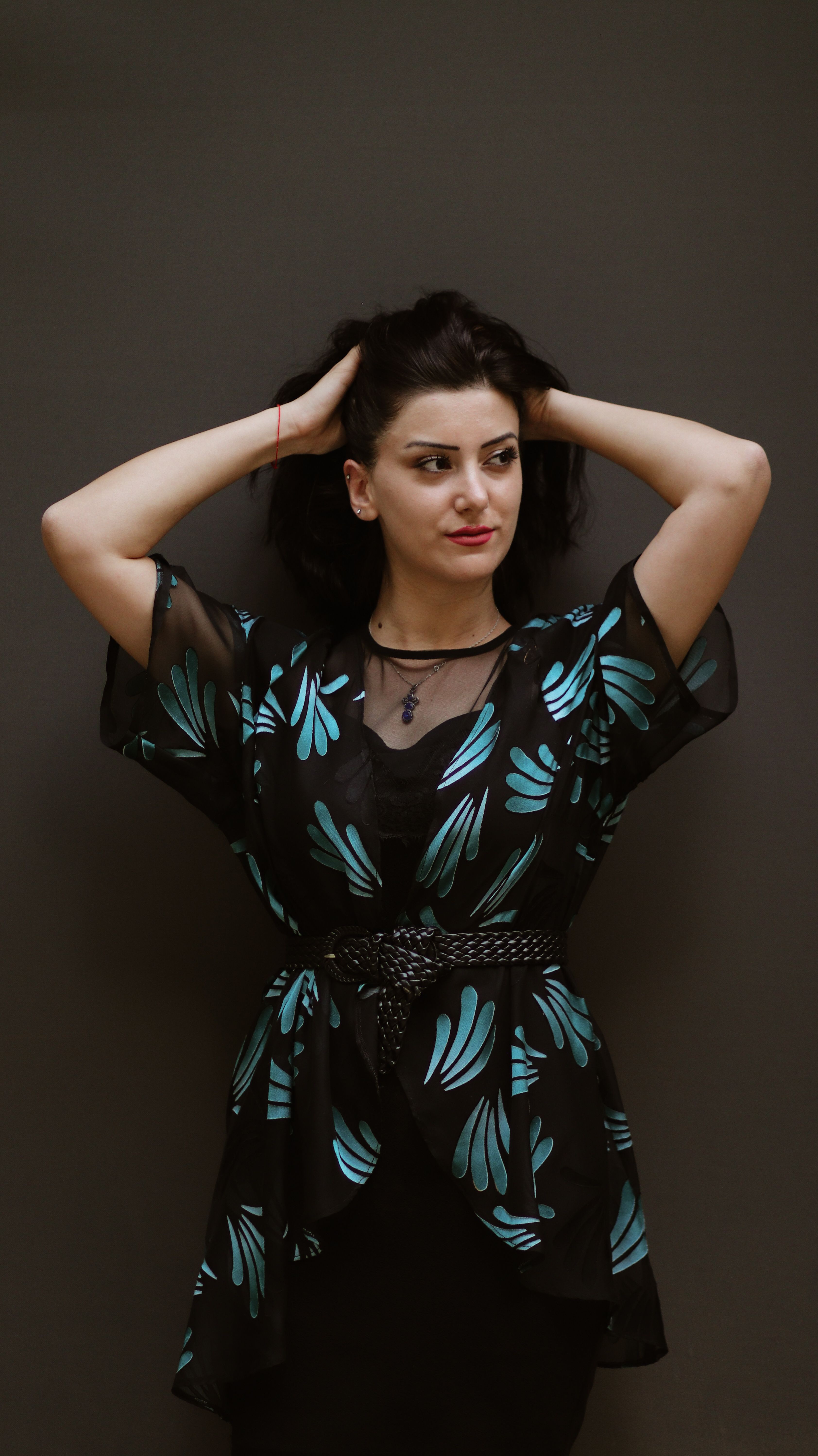 Stylish woman with floral dress posing with hands on hair against a dark backdrop.