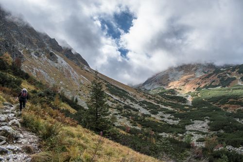 Free Woman hiking on a scenic rocky trail in mountainous terrain under a cloudy sky. Stock Photo