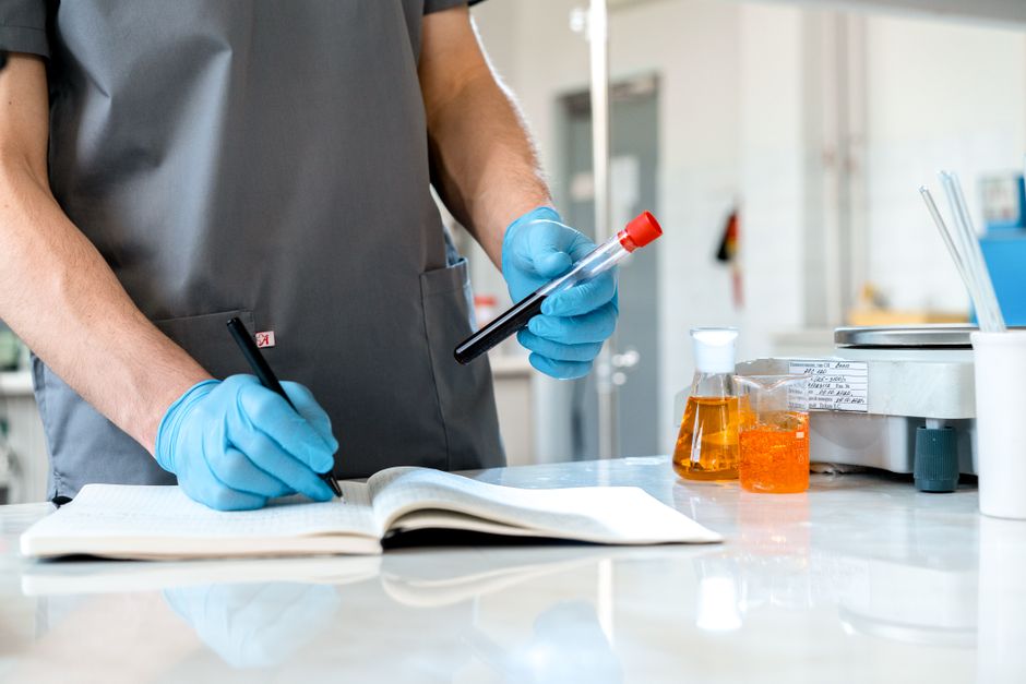 Scientist writing observations in lab notebook while holding a test tube