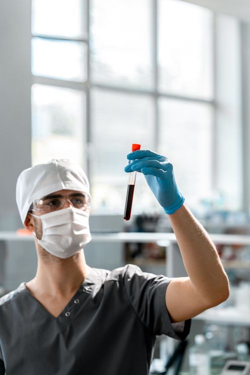 Free Scientist in protective gear examining a test tube with a blood sample in a bright laboratory. Stock Photo