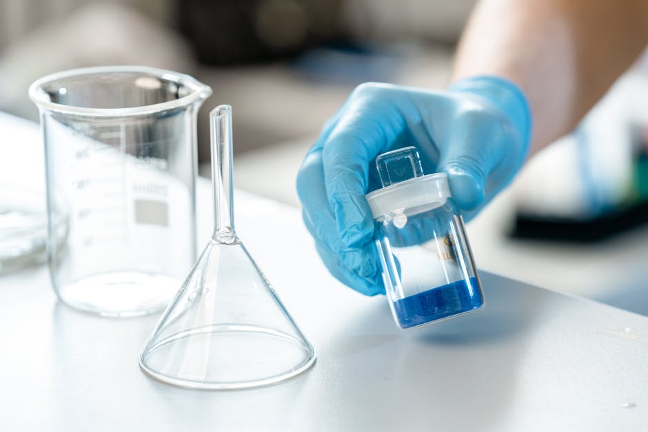 Scientist holding vial with blue liquid next to beaker and funnel in lab.