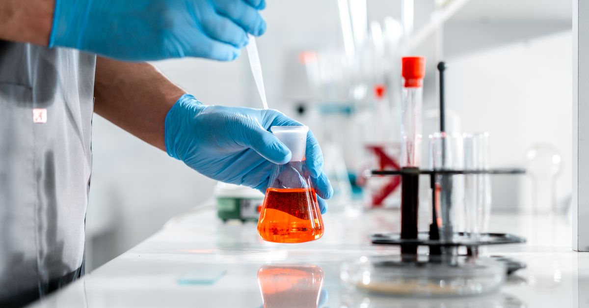 Ilmuwan sedang bekerja hati-hati dengan labu Erlenmeyer dan pipet di lingkungan laboratorium.