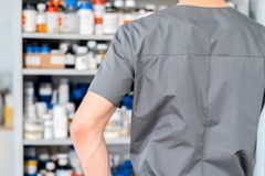 Male pharmacist in surgical cap and gloves organizing shelves of medication in a pharmacy.