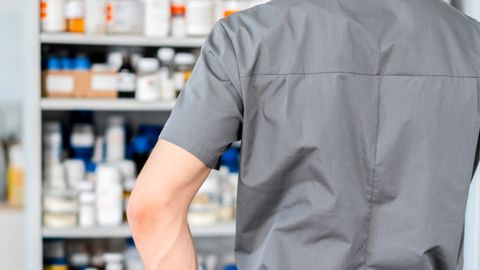 Male pharmacist in surgical cap and gloves organizing shelves of medication in a pharmacy.