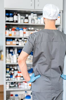 Male pharmacist in surgical cap and gloves organizing shelves of medication in a pharmacy.