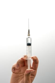 A detailed view of a human hand holding a medical syringe against a white background.