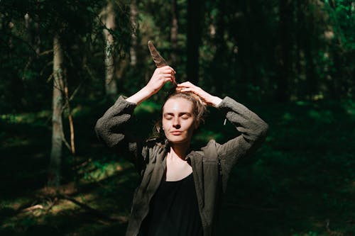 Young Woman Standing with Eyes Closed in a Forest and Holding a Feather 