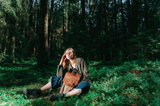 A woman sits peacefully in a sunlit forest, holding a leather backpack, enjoying nature.