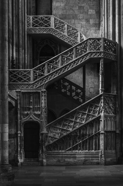 A black and white image of a Gothic-style spiral staircase in Rouen Cathedral, France.
