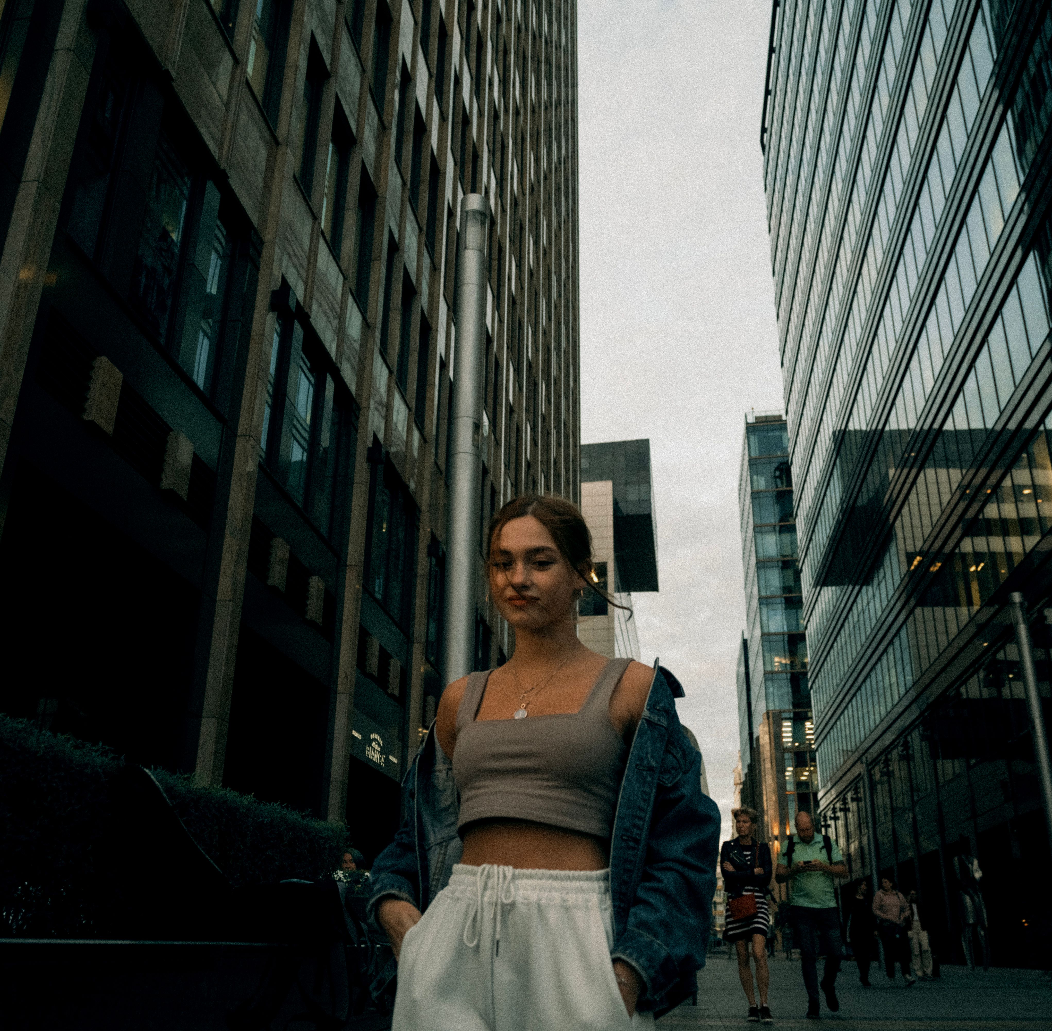Woman in Crop Top with Denim Jacket Walking on the Street Between High ...