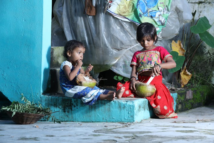 Young Girls Sitting On Concrete Step While Eating Coconut Fruit