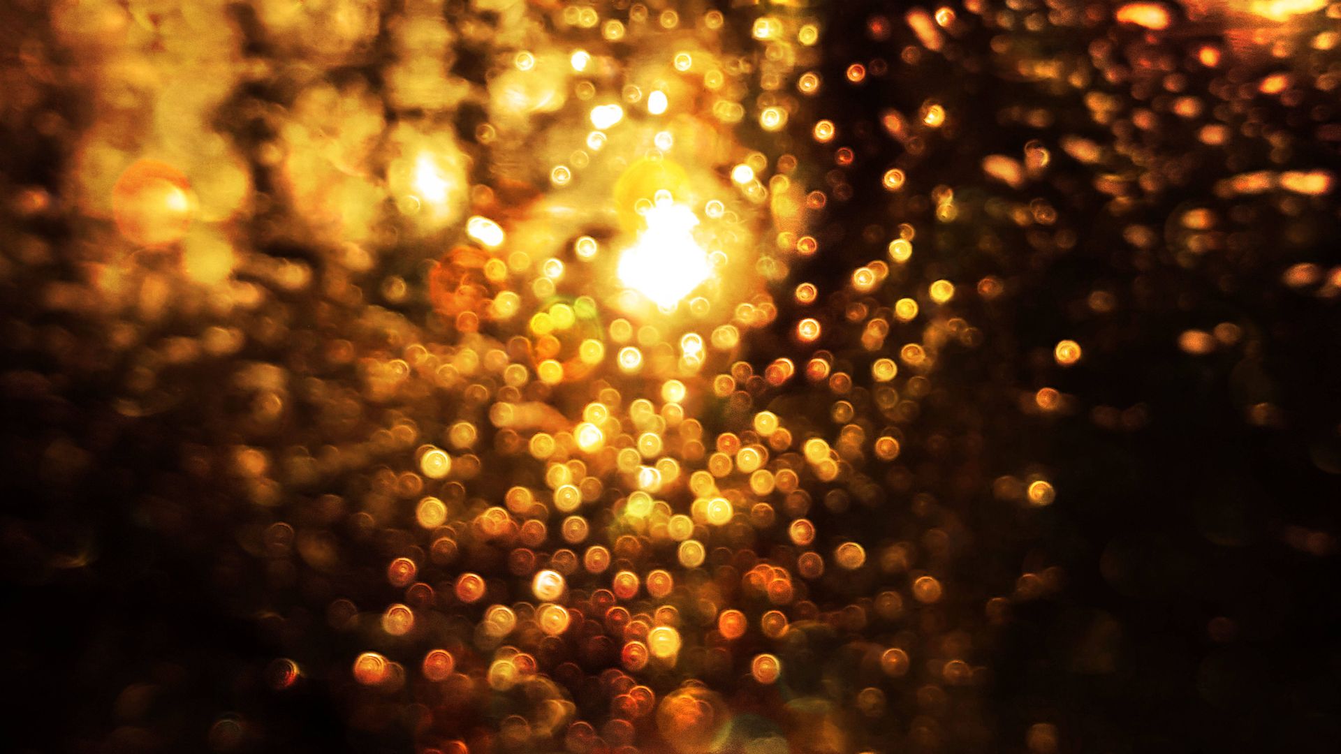 Abstract bokeh image with warm gold tones and raindrop effect, showcasing a sparkling light arrangement.