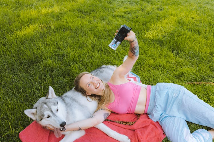 A Woman Using A Video Camera While Lying Beside Her Pet Dog