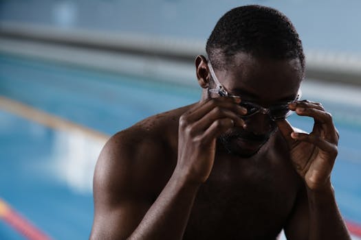 A focused athlete preparing for swimming in an indoor pool by adjusting his goggles.