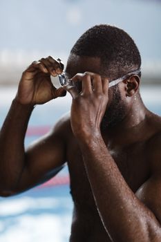 Close-up of a male swimmer adjusting his goggles before training in an indoor pool setting.