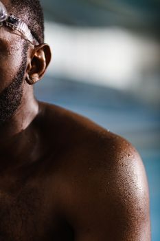 Close-up of a shirtless swimmer with water droplets, highlighting athletic strength.