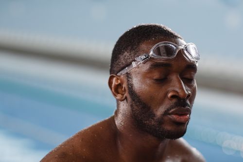 Free Close-up of a black swimmer with goggles in a pool, eyes closed in focus. Stock Photo