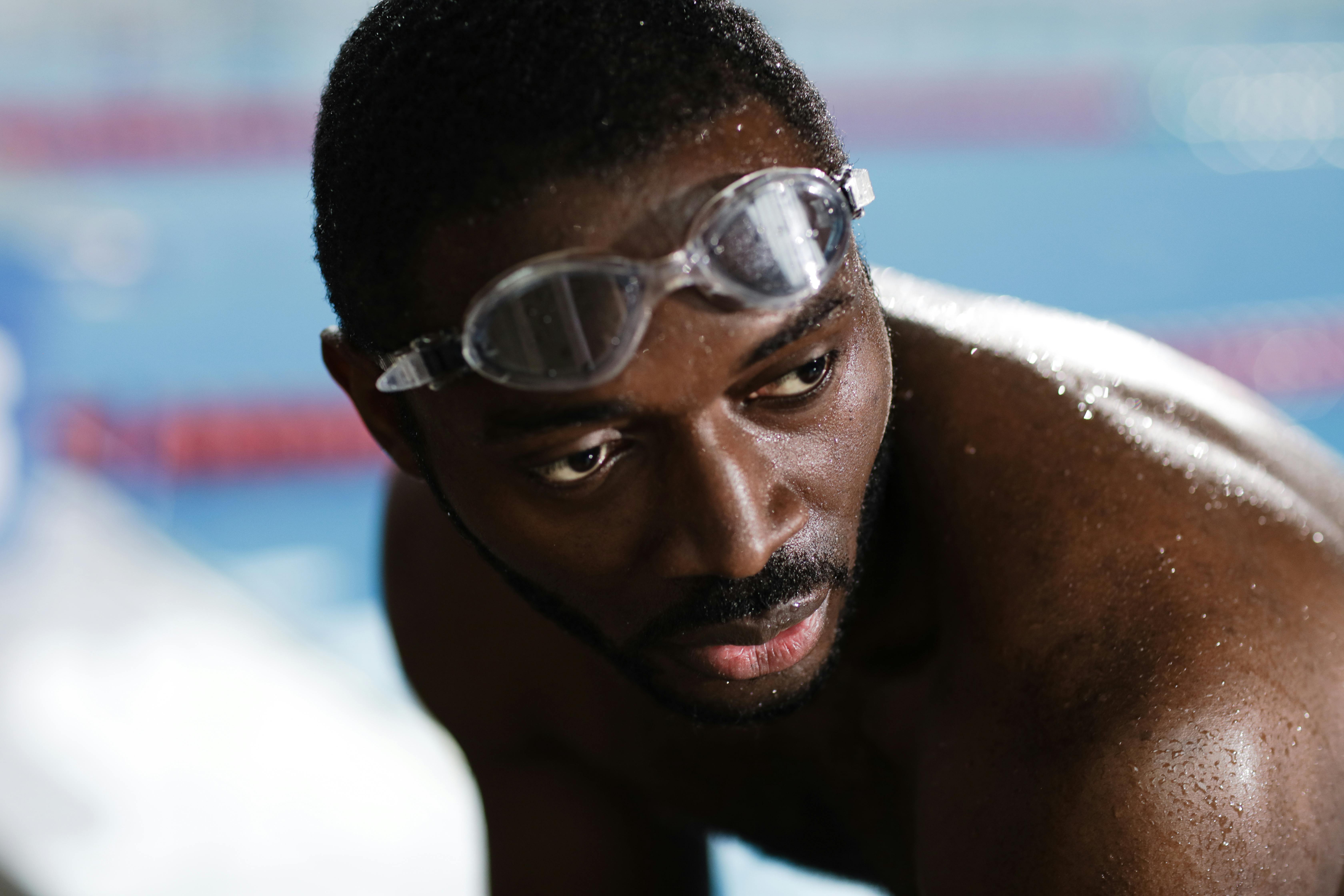 Focused African American swimmer with goggles near the pool edge.