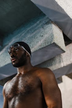 Portrait of a shirtless adult swimmer with goggles and swim cap indoors.