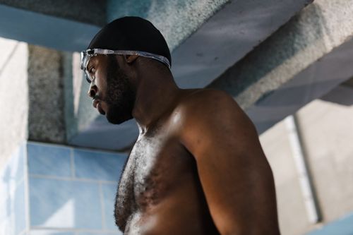 Free Low angle view of a topless male swimmer wearing goggles and swim cap indoors. Stock Photo