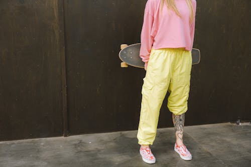 Person Wearing Pink Long Sleeve Shirt and Yellow Pants Holding a Skateboard