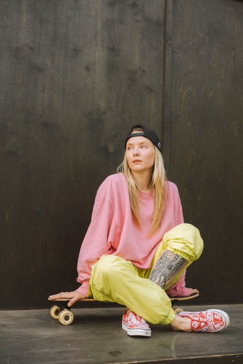 Free Tattooed woman in casual attire sitting with skateboard indoors. Stock Photo