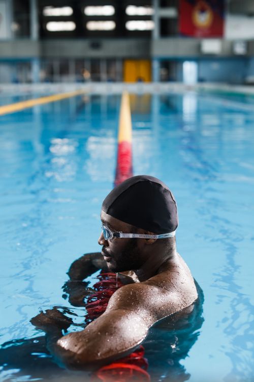 Free Bearded male swimmer rests against lane rope in a bright indoor pool setting. Stock Photo