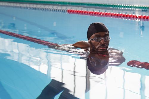 Free Close-up of a man swimming in an indoor pool, wearing a swim cap and goggles. Stock Photo