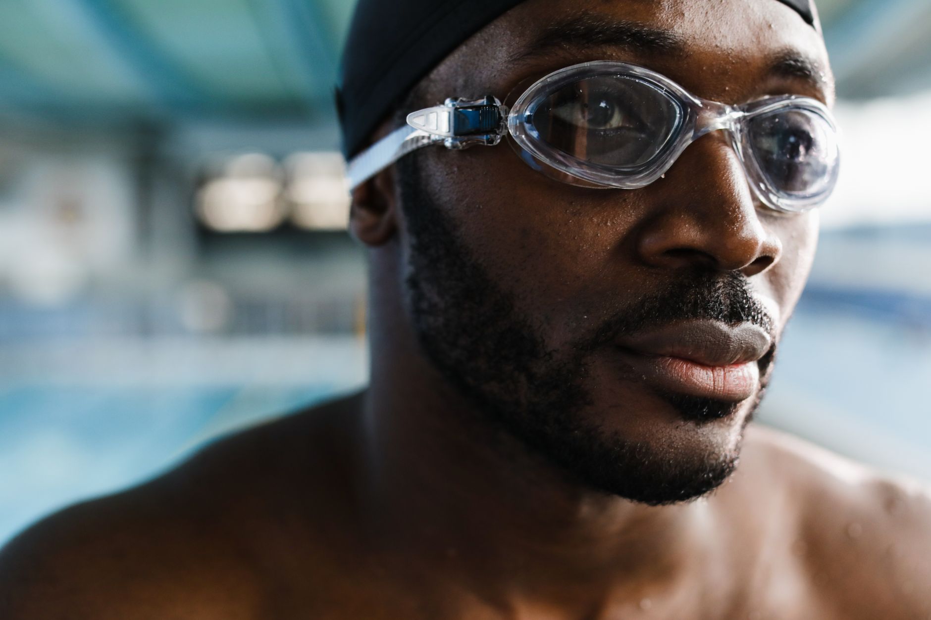 Close-up portrait of a determined male swimmer with goggles, preparing for a swim in an indoor pool.