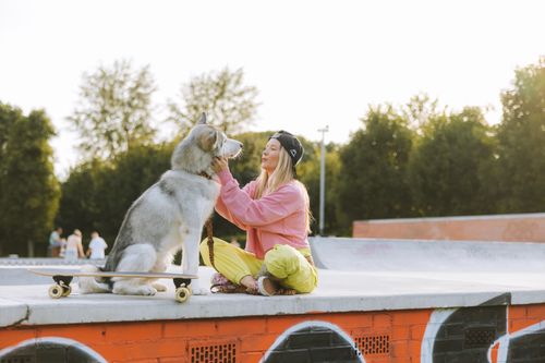 Free A young woman sits with her Siberian Husky and a longboard at an outdoor skatepark. Stock Photo