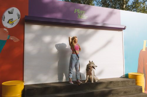 Free A woman in casual attire stands with a husky dog on urban concrete steps, showcasing a vibrant and playful street scene. Stock Photo
