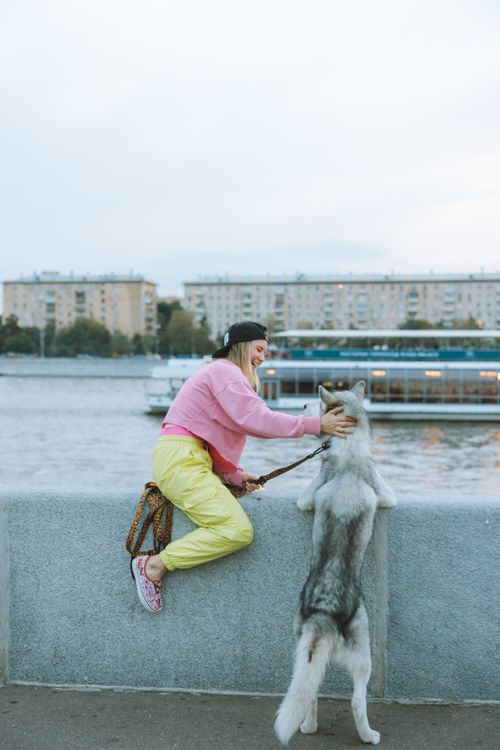 Free Woman in colorful attire pets Siberian Husky by the riverbank, enjoying a peaceful outdoor moment. Stock Photo