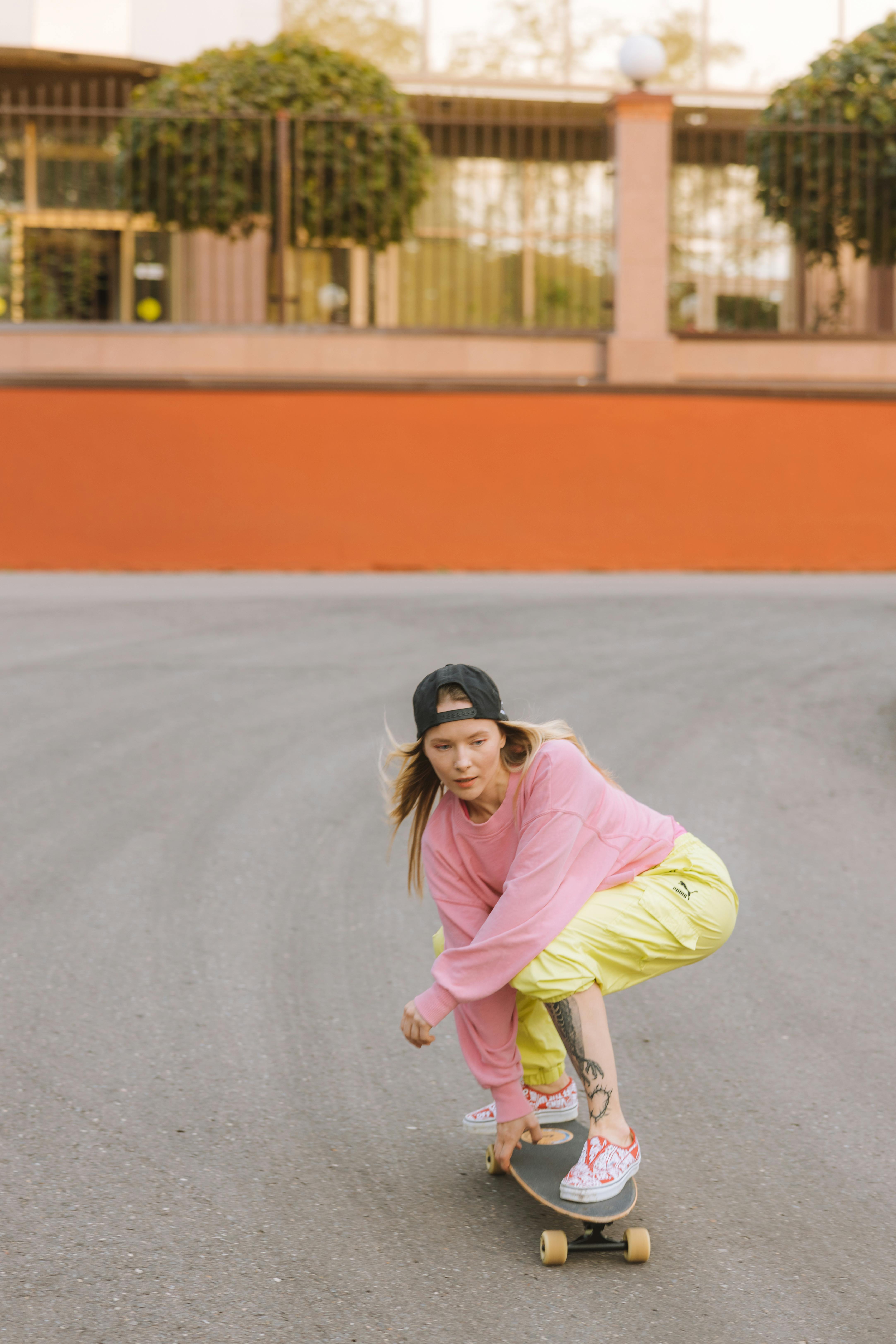 A young woman wearing colorful casual clothes skateboarding outdoors on a smooth road.